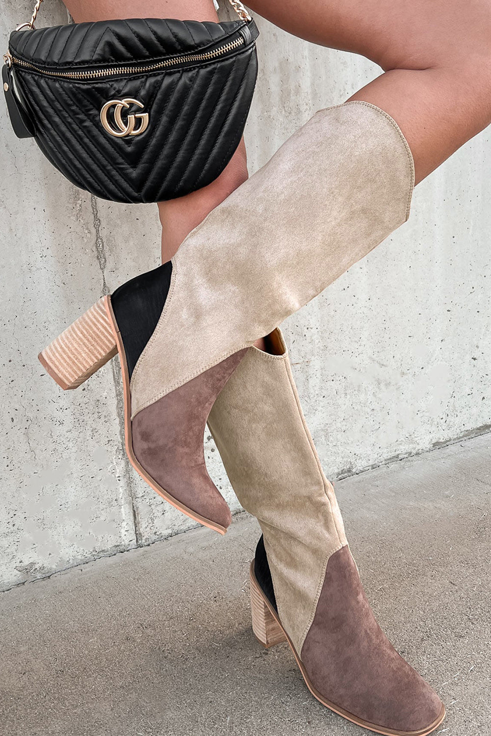 Person wearing beige and brown suede boots with a black bag featuring a gold logo.