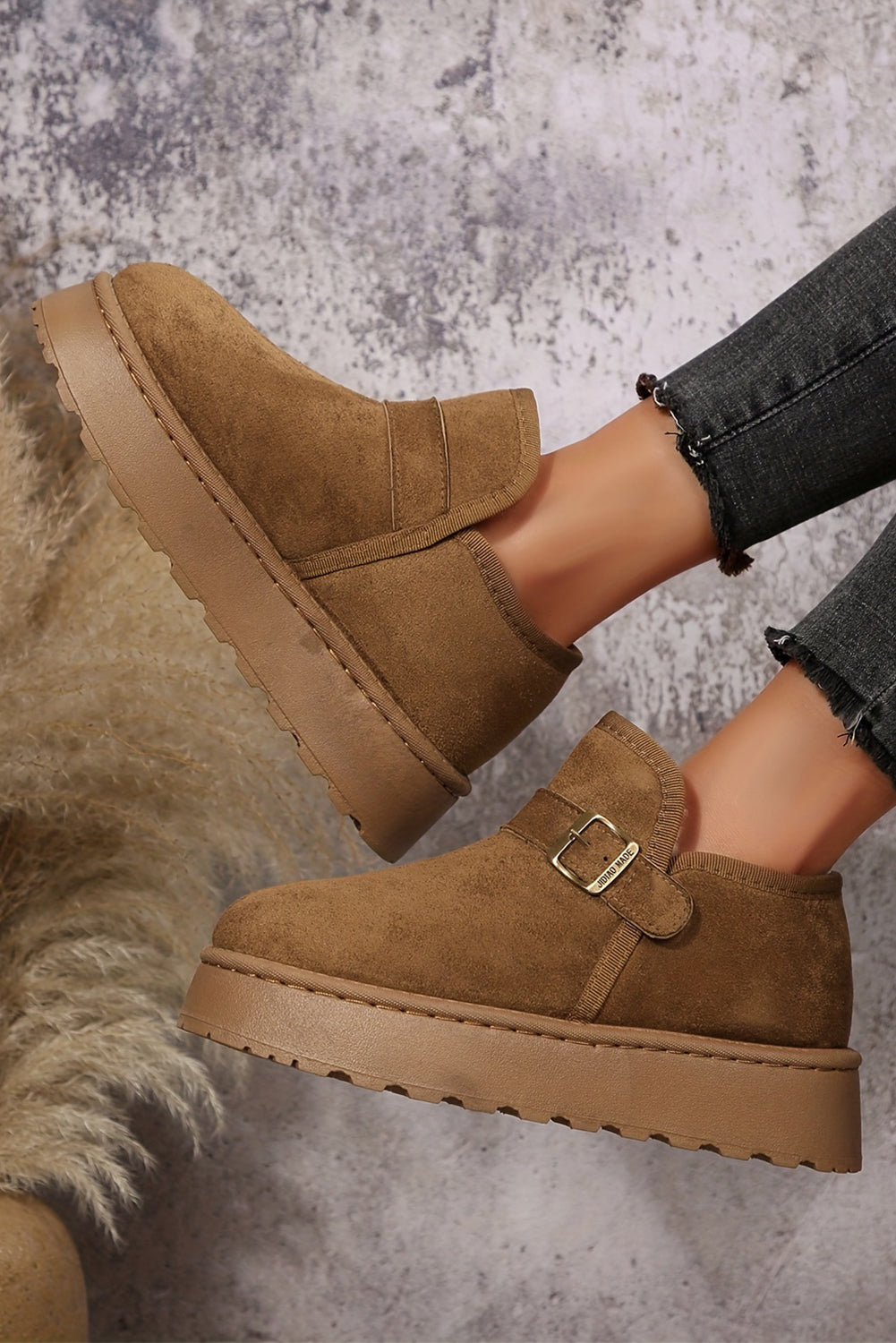 Brown suede boots with a buckle on a textured gray background