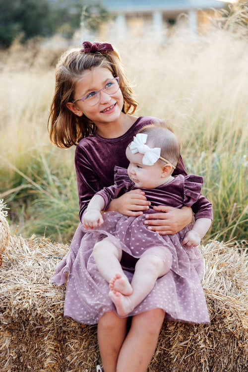 Two young girls in matching dresses sitting on a hay bale in a field.