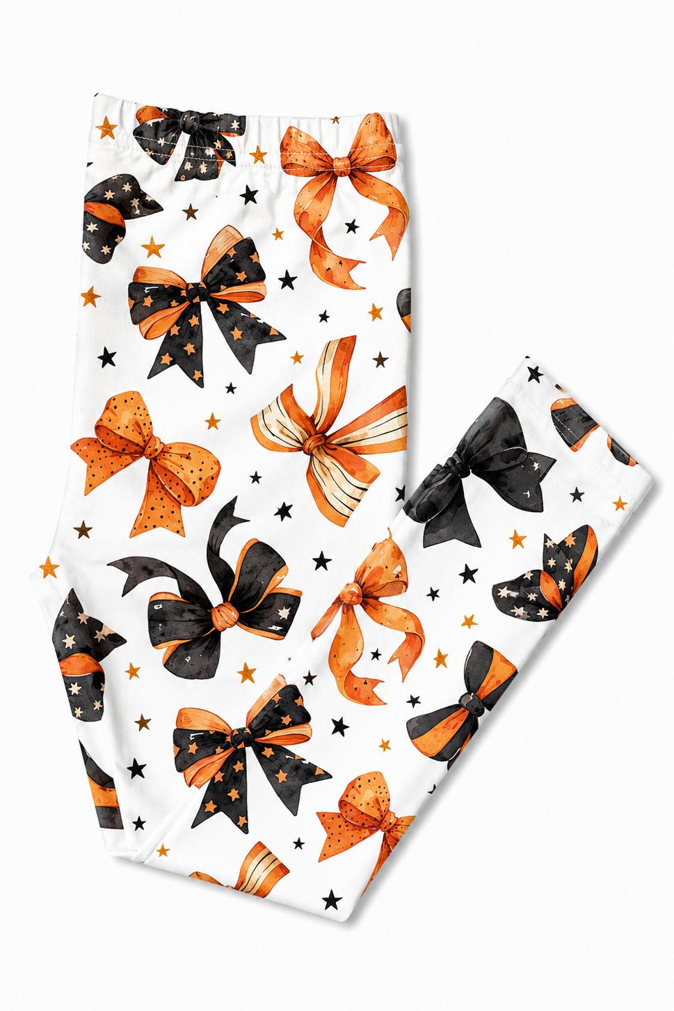 White children's leggings with a festive pattern of orange and black bows and small stars, shown on a clean white background.