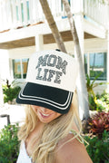 Woman wearing a cap with 'Mom Life' text in an outdoor setting