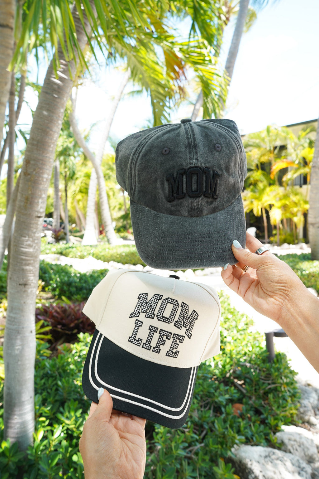 Two hats held up against a tropical background with palm trees.
