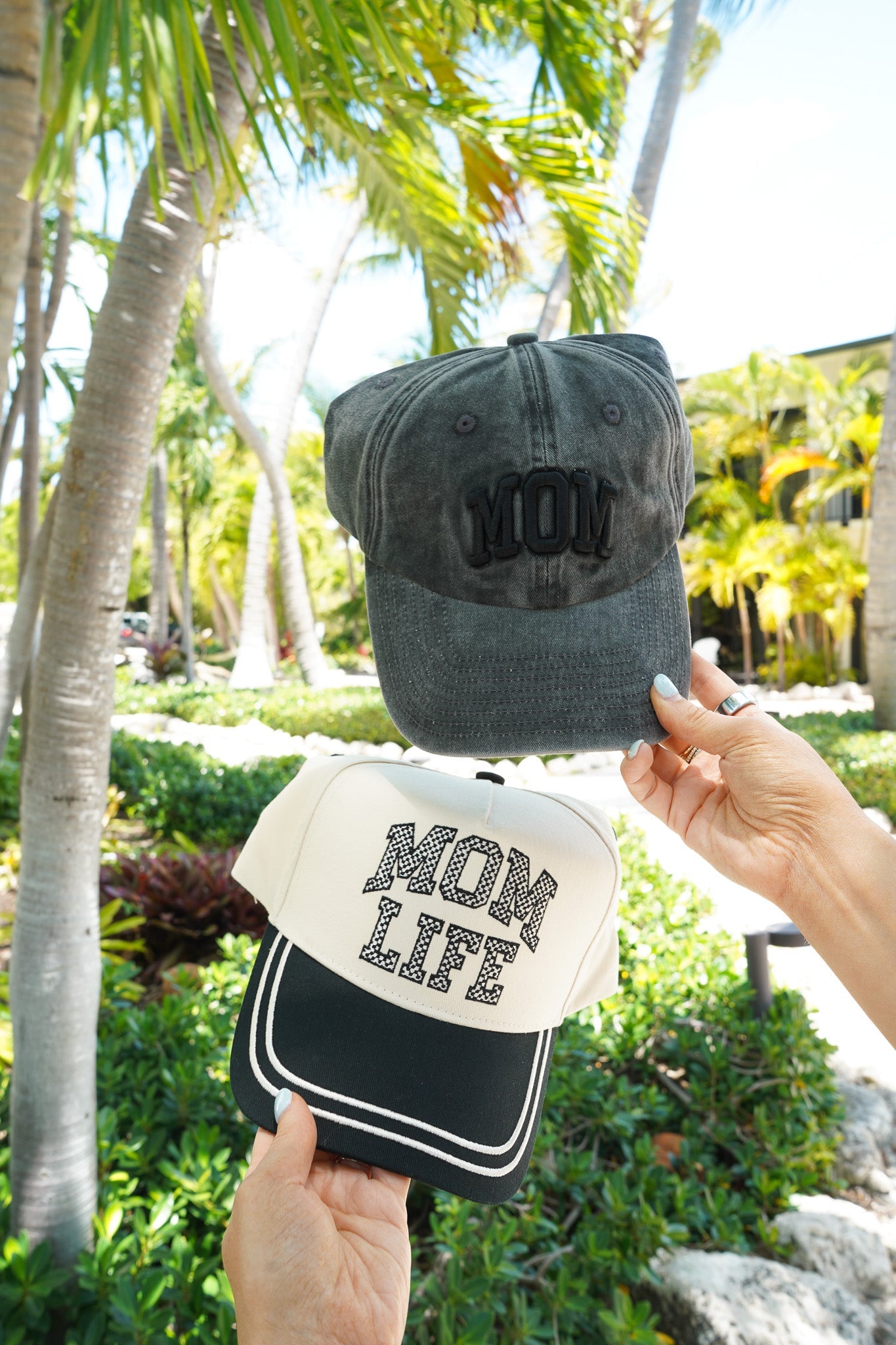 Two hats held up against a tropical background with palm trees.