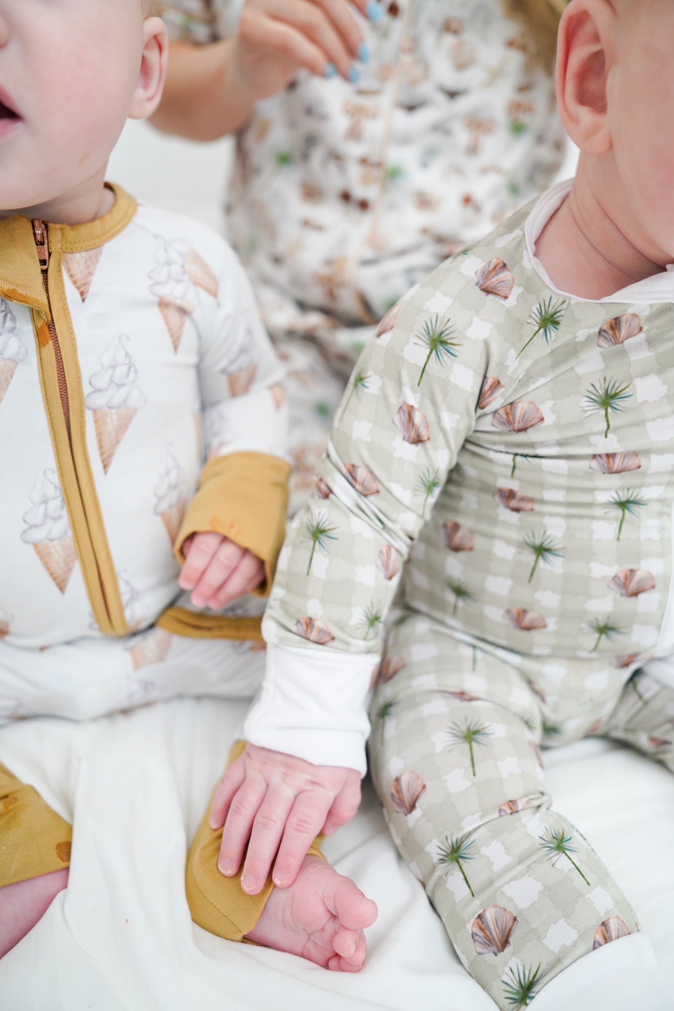 Two babies wearing patterned pajamas sitting close together on a white blanket.