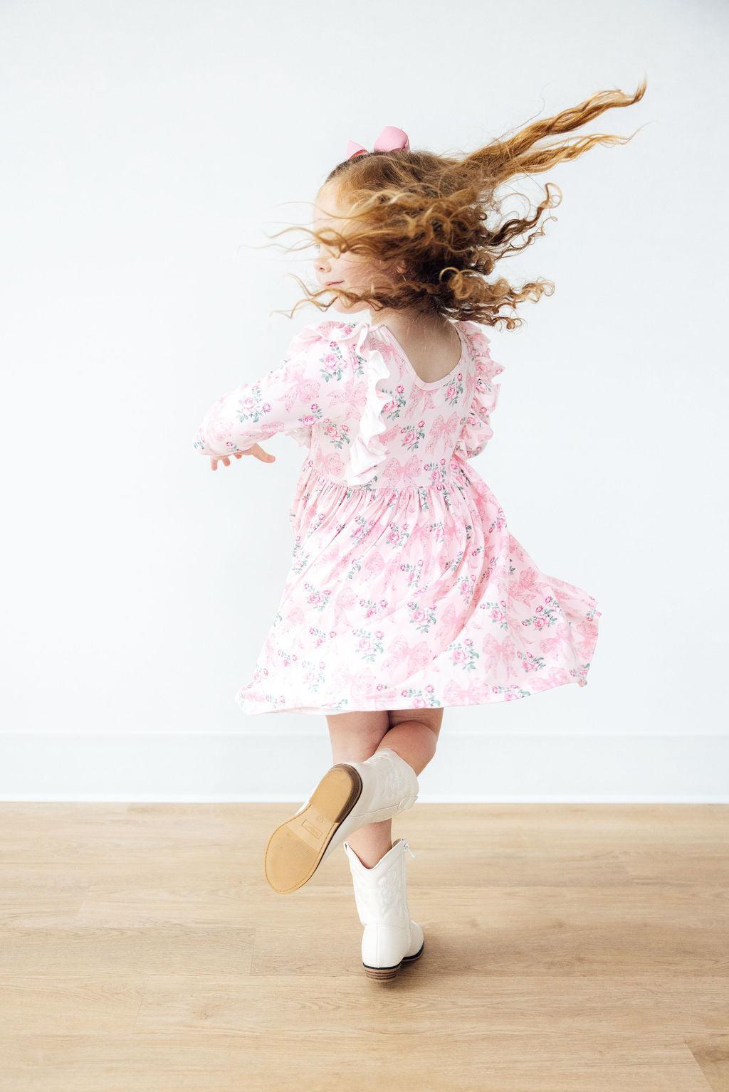 Child in a pink floral dress and white boots running on a wooden floor with a white background