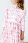 Child wearing a pink floral dress with ruffled sleeves against a white background