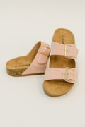 A pair of pink double-strap slide sandals with gold-tone buckles and cork soles, photographed on a clean white background.