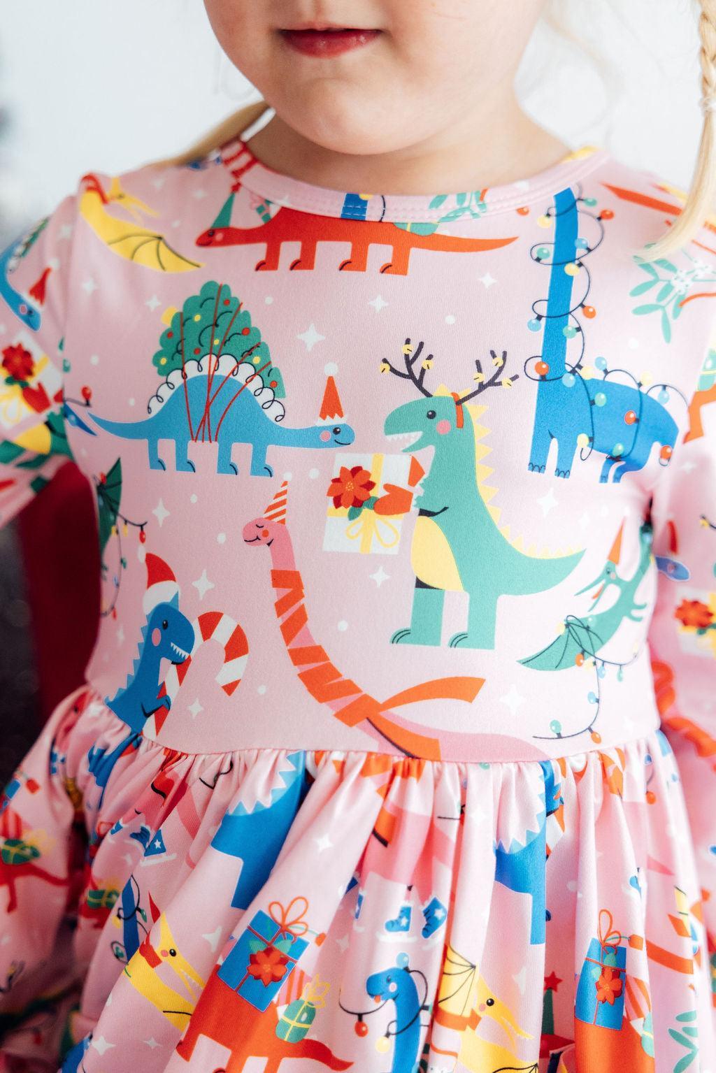 Child wearing a dress with colorful dinosaur patterns on a light background