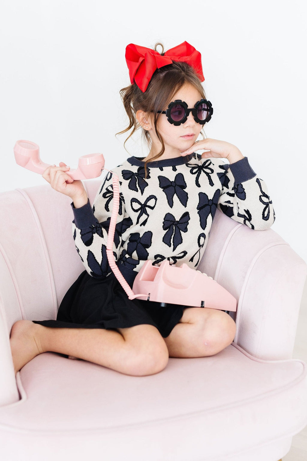 Child wearing a black and white patterned sweater with bows, sitting on a pink couch.