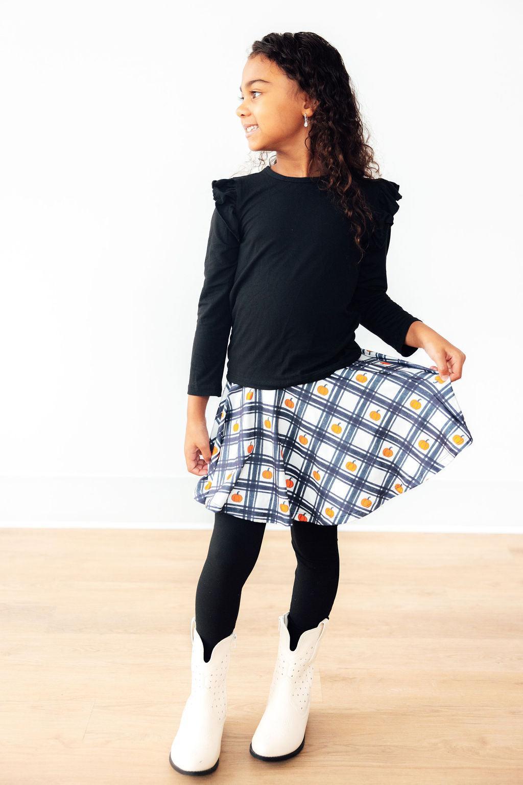 Young girl wearing a black top and plaid skirt on a white background