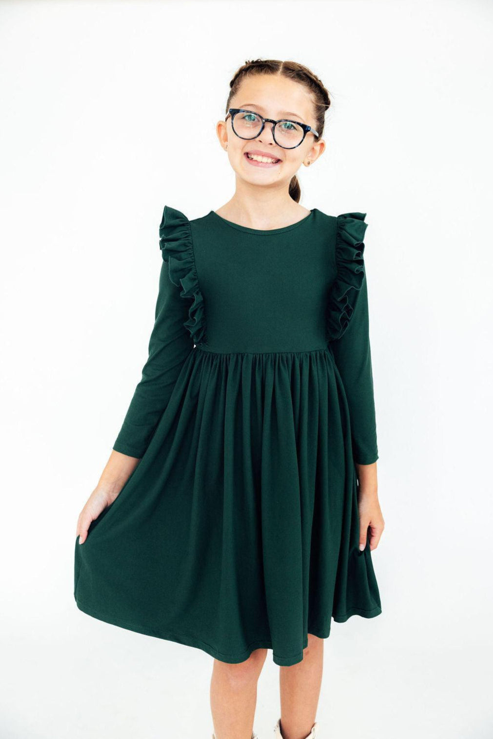 Young girl wearing a green dress with ruffled sleeves on a white background