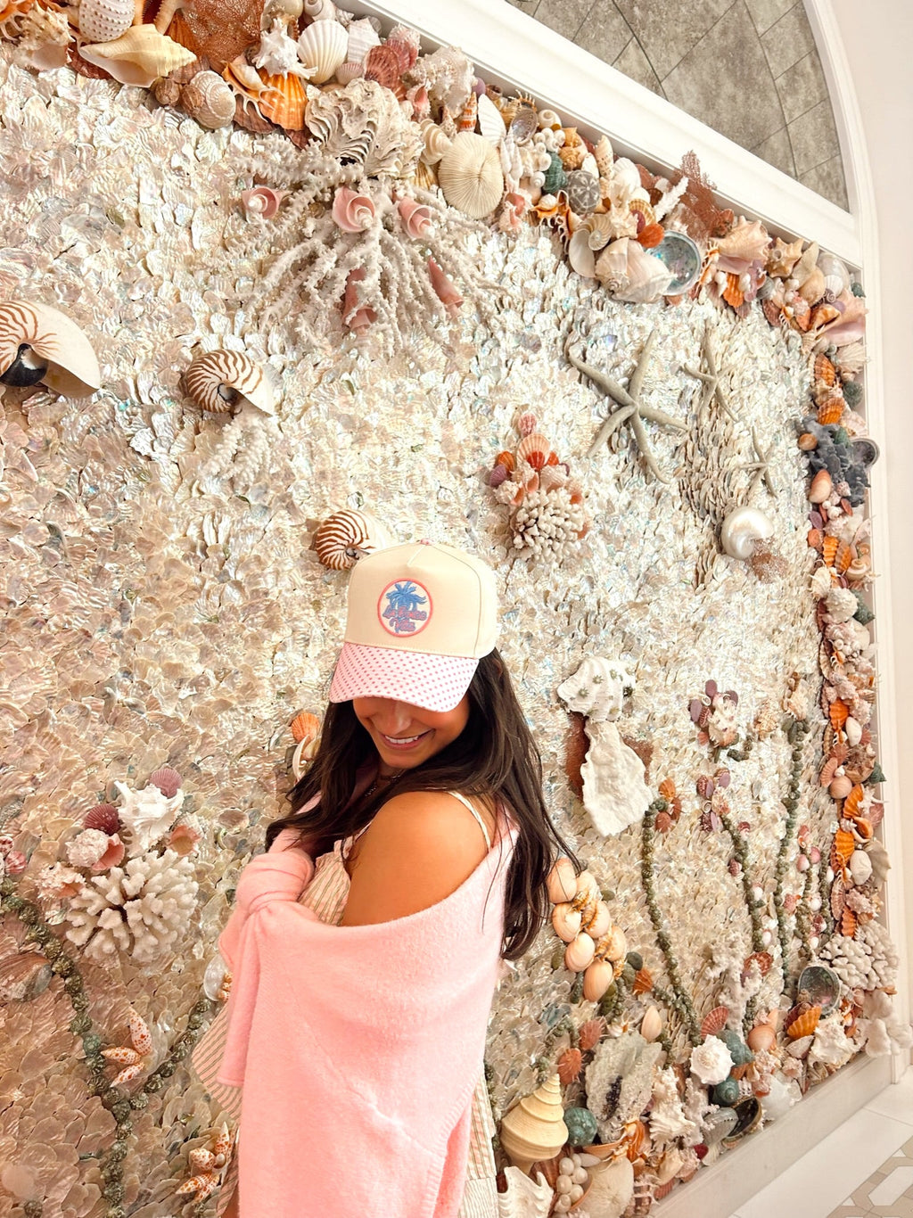 Woman posing in front of a wall decorated with seashells and starfish