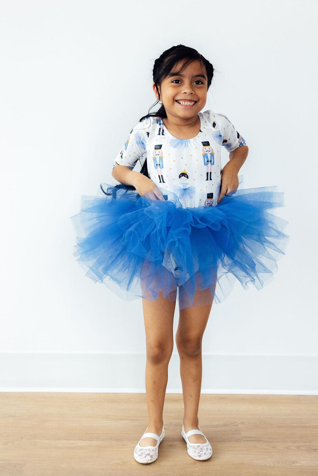 Child wearing a blue tutu skirt with a white background