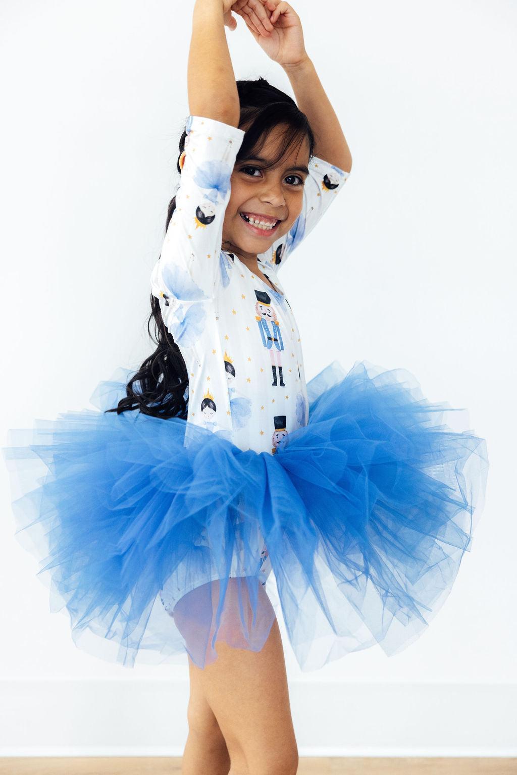 Child wearing a blue tutu and white outfit with cartoon characters on a white background