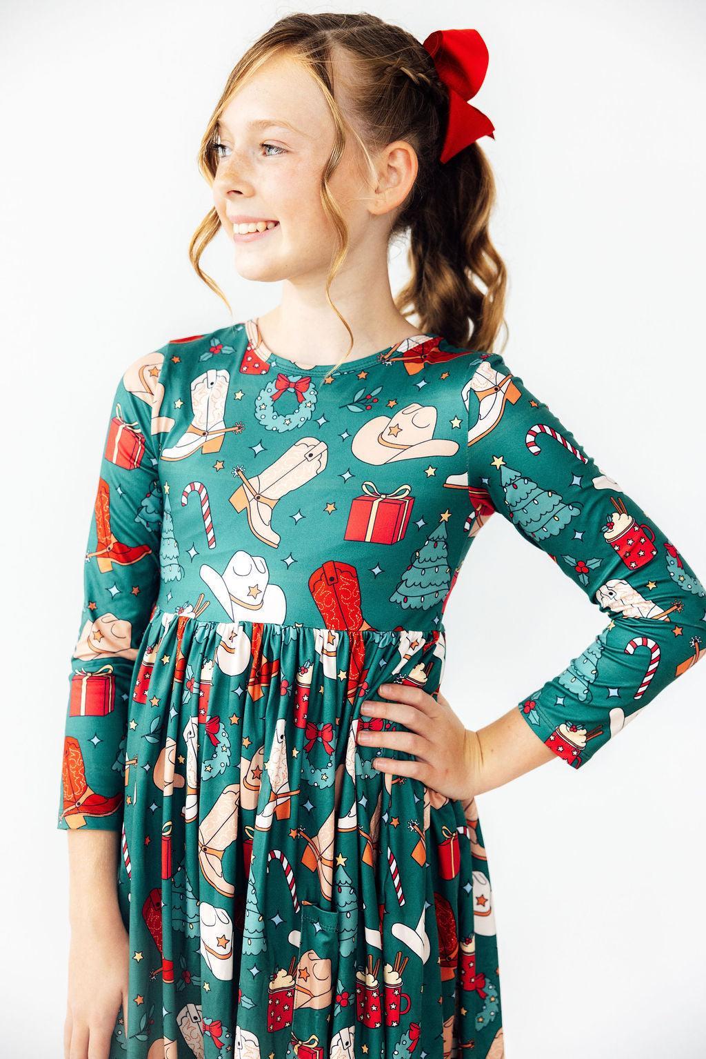 Young girl wearing a festive dress with Christmas-themed pattern on a white background