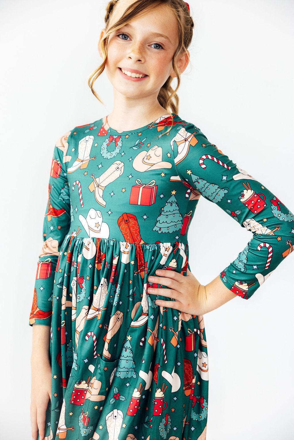 Young girl wearing a festive green dress with Christmas-themed patterns on a white background