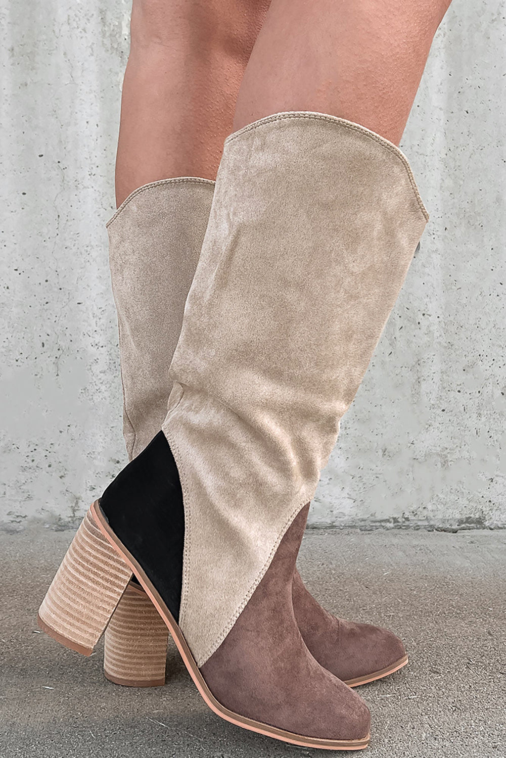 Beige and brown knee-high boots on a concrete floor with a gray wall background