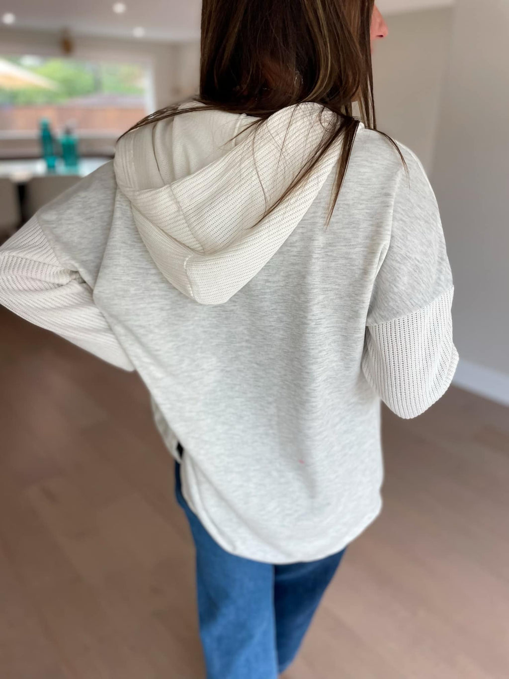 Person wearing a light gray hoodie with a hood indoors