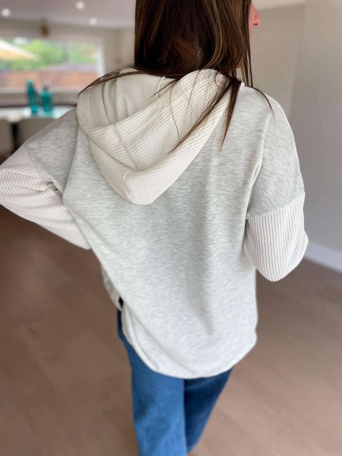 Person wearing a light gray hoodie with a hood indoors