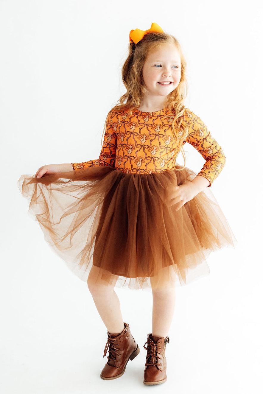 Young girl wearing an orange dress with a tulle skirt on a white background