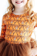 Child wearing an orange dress with a pattern of turkeys and bows, standing against a white background.
