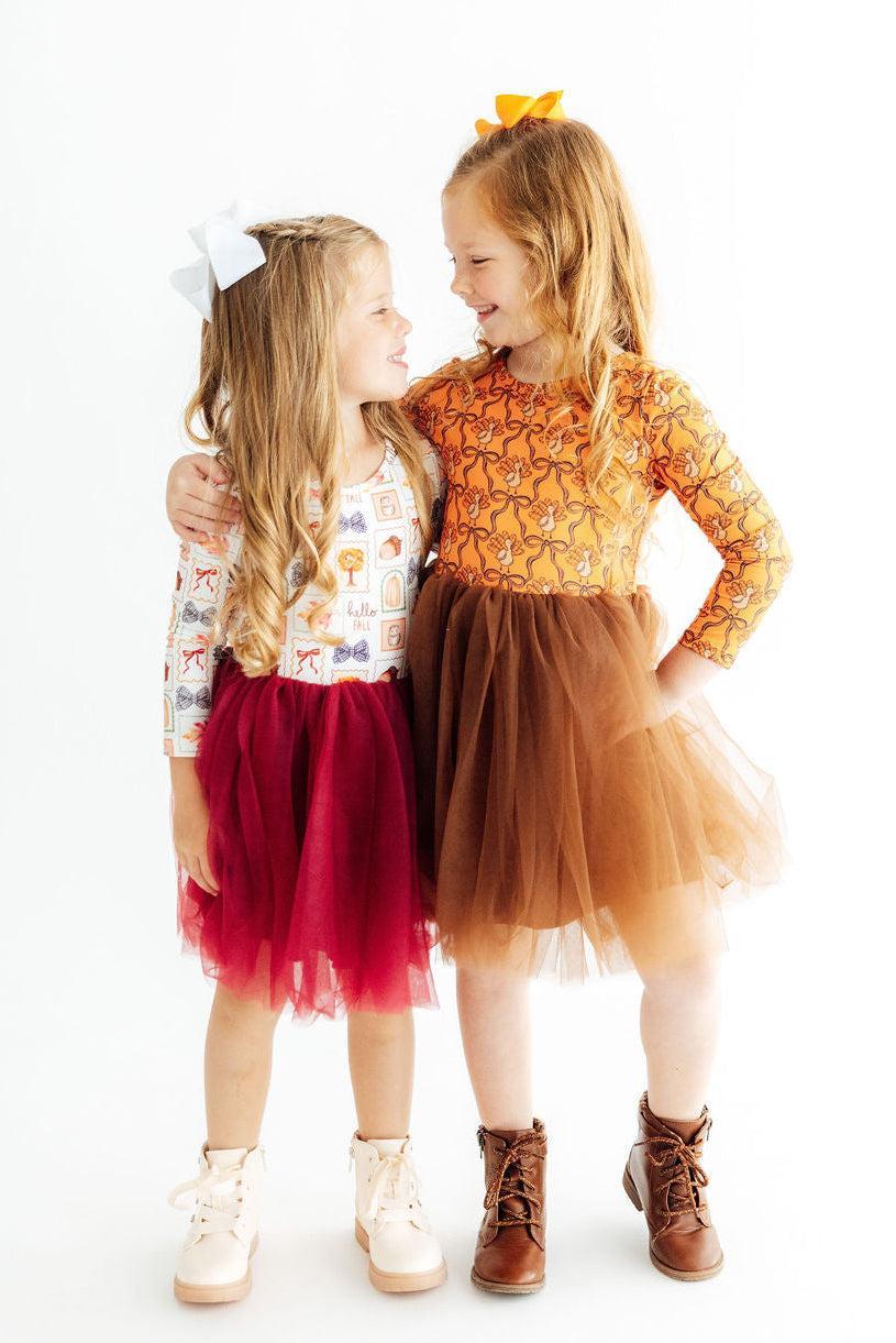Two young girls in colorful dresses standing close together on a white background